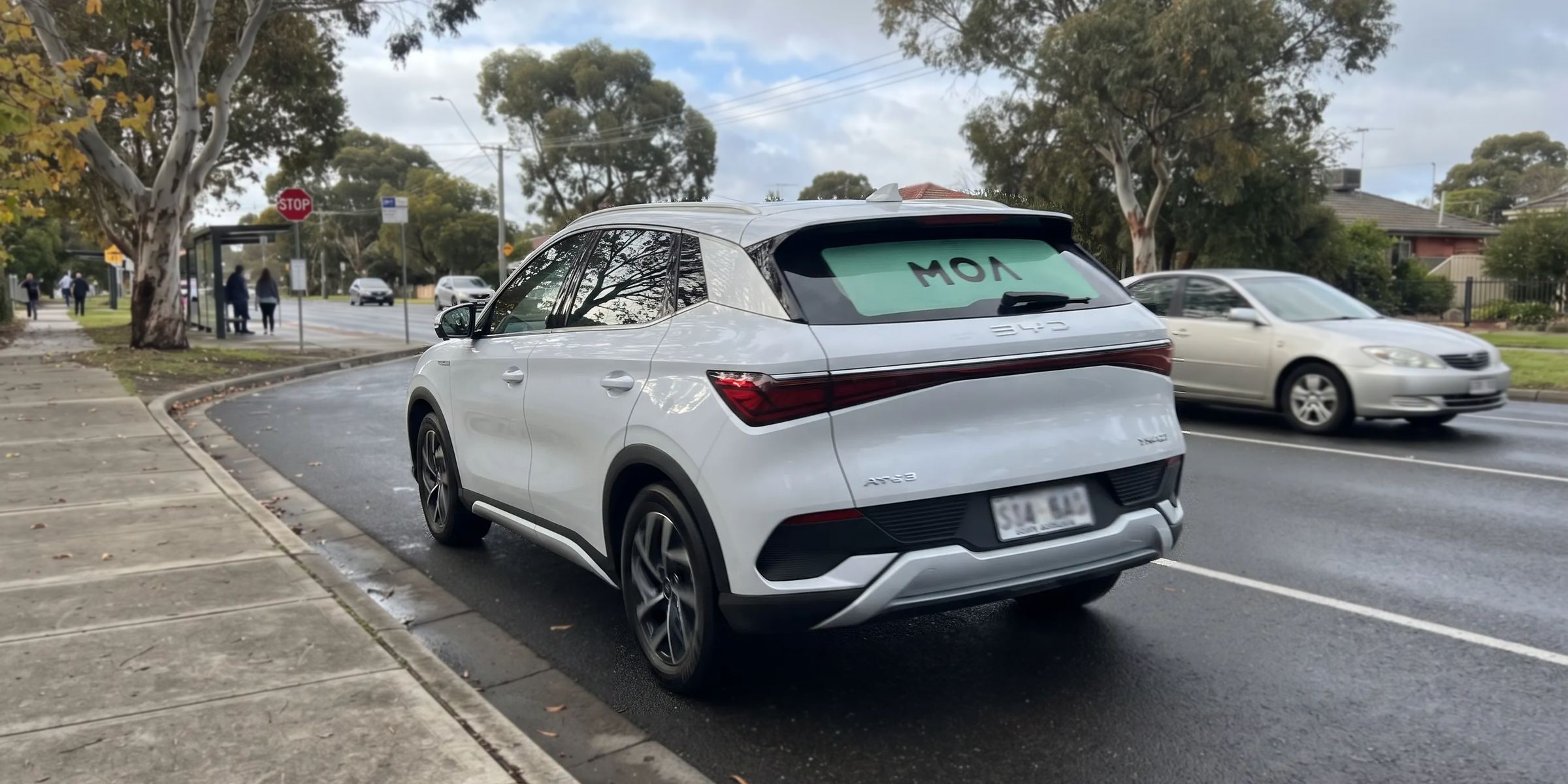 MOA branded white SUV on a suburban street beside a bus stop