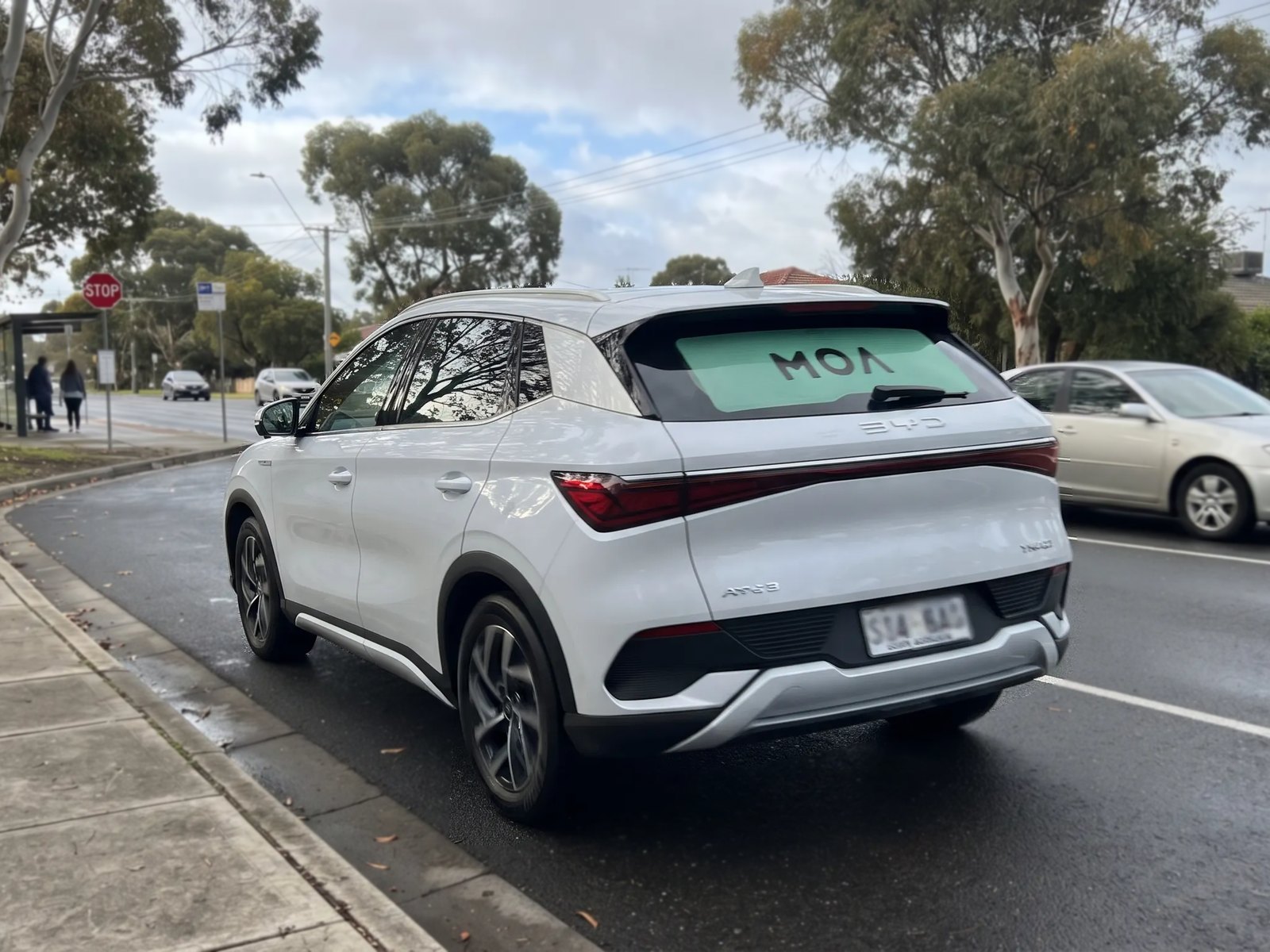 MOA branded white SUV pulling away from a suburban bus stop