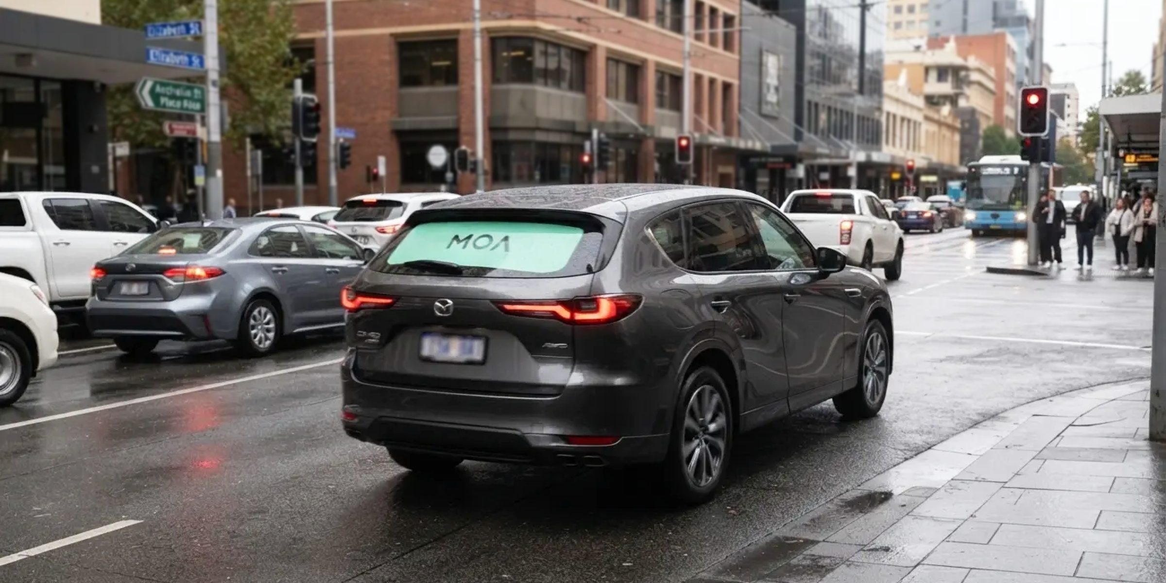 MOA branded SUV with a mint rear window ad moving through busy city traffic beside buses