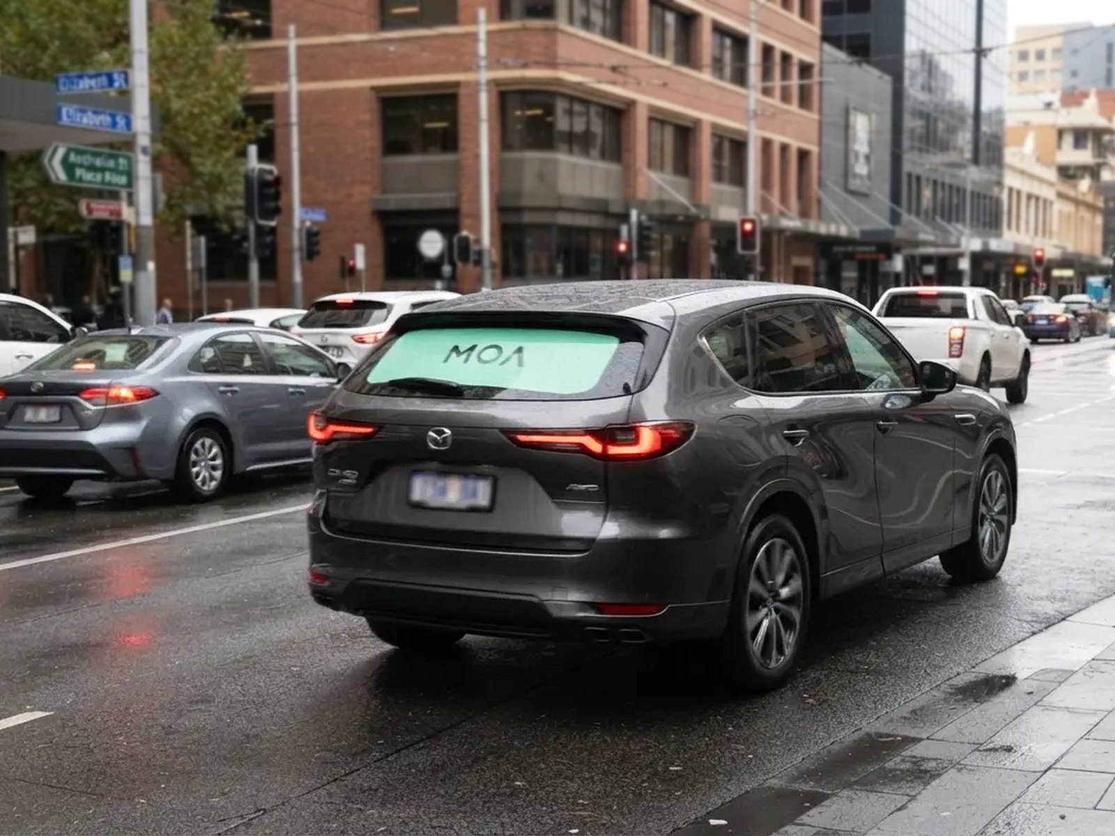 MOA branded SUV waiting at city traffic lights, rear window ad visible