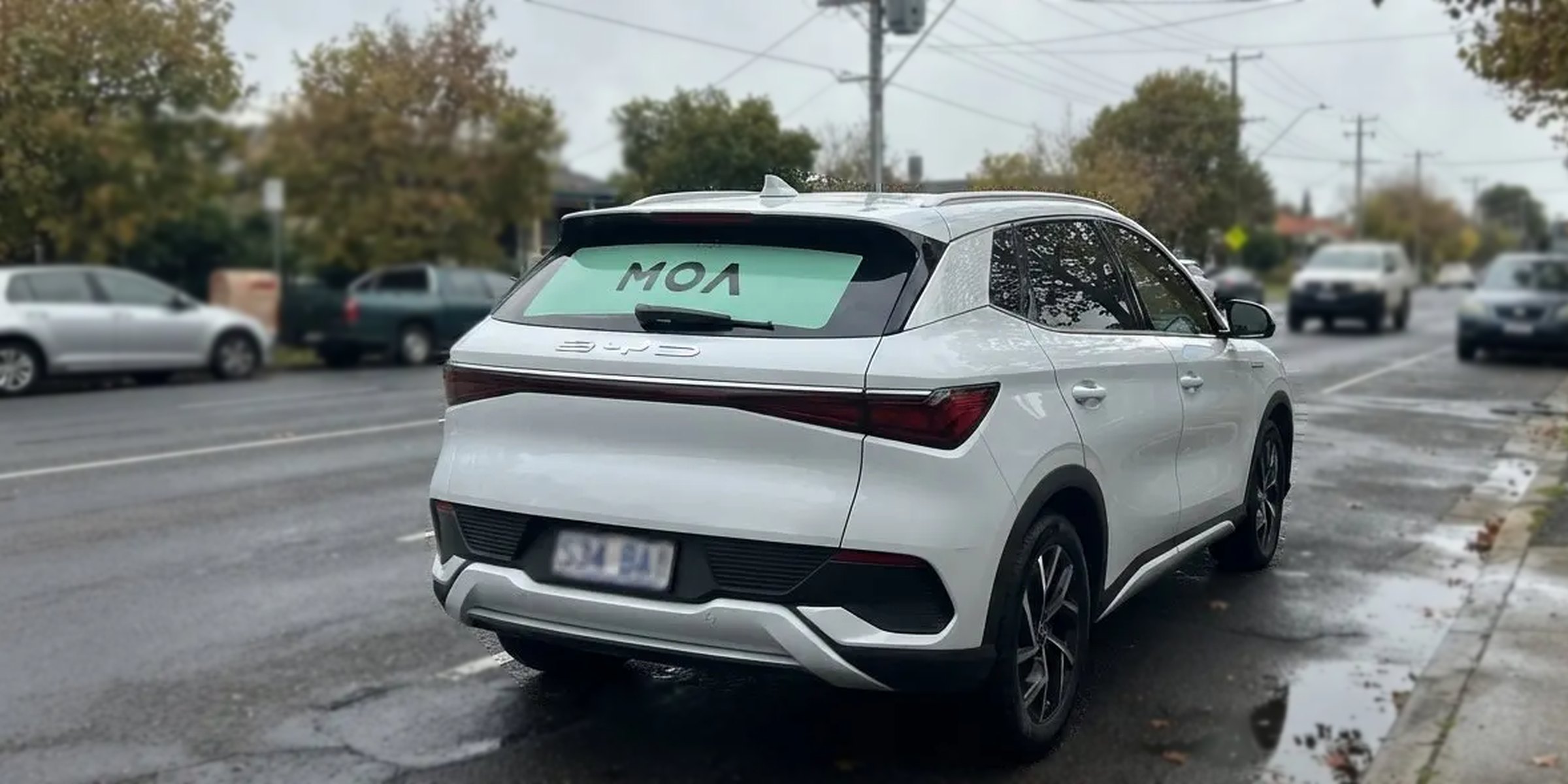 MOA branded white SUV on a quiet tree lined suburban street
