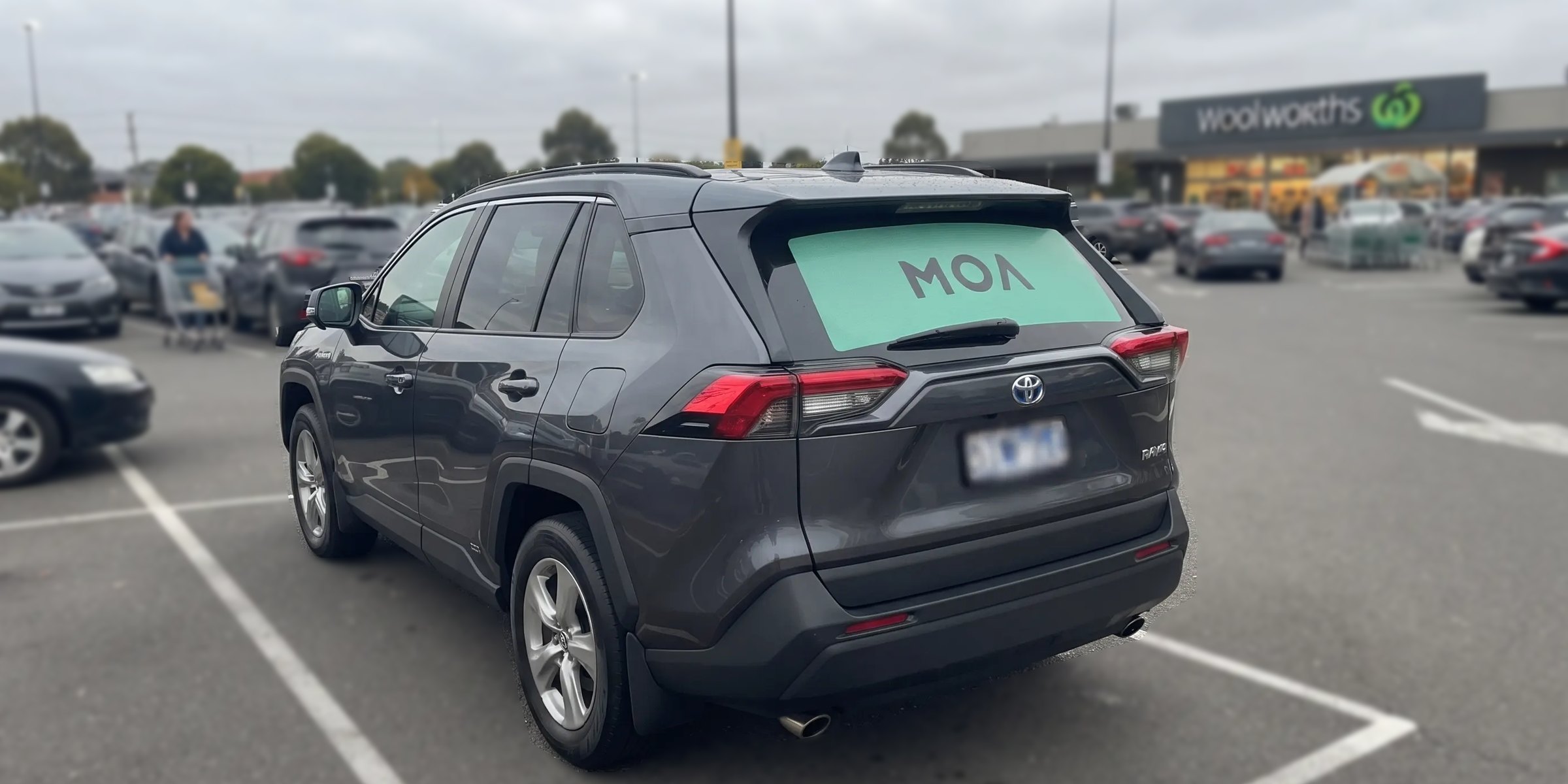 MOA branded SUV parked in a suburban supermarket car park, mint rear window ad visible