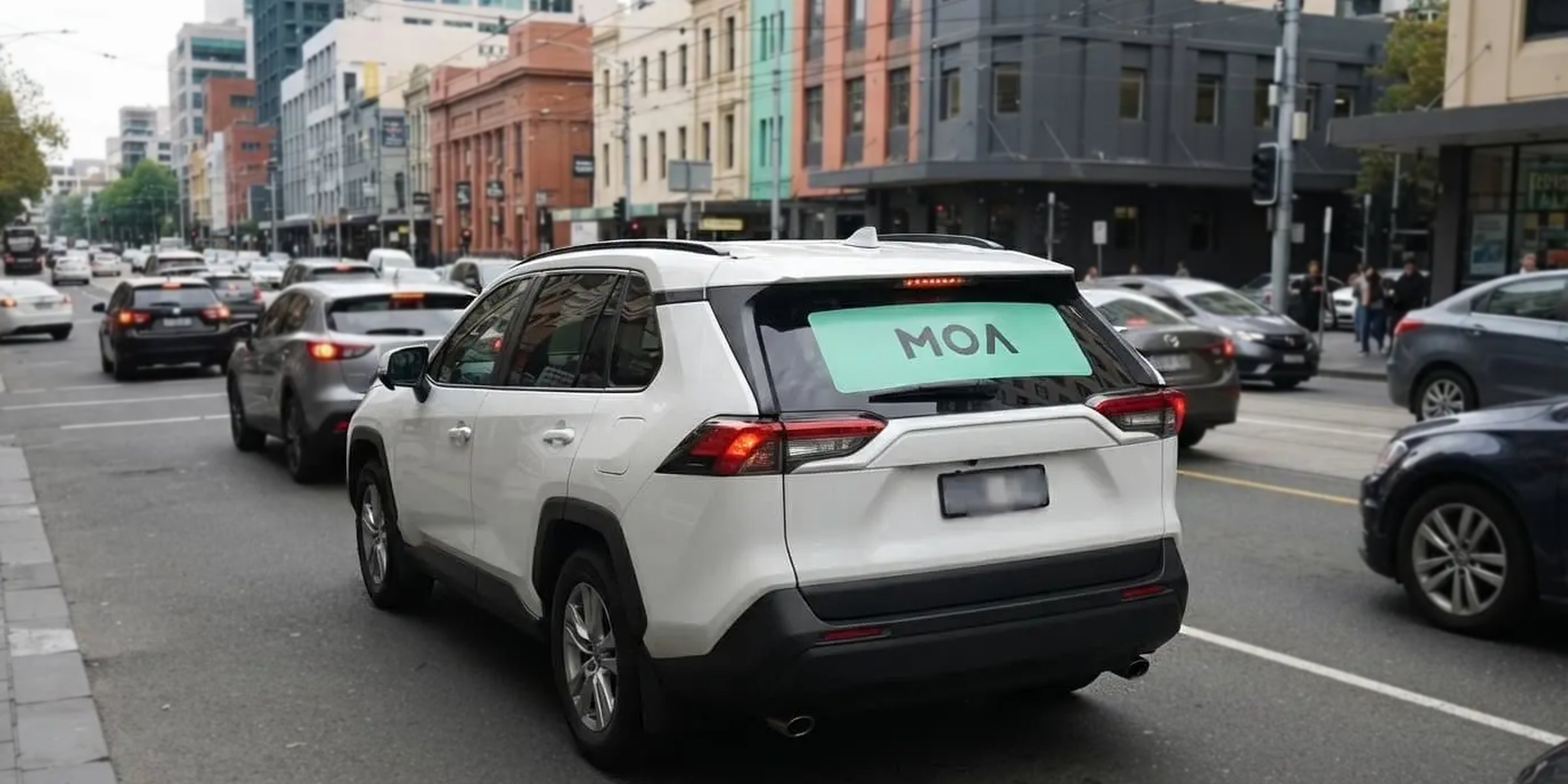 MOA branded white SUV in queued city traffic, mint rear window ad visible to the cars behind