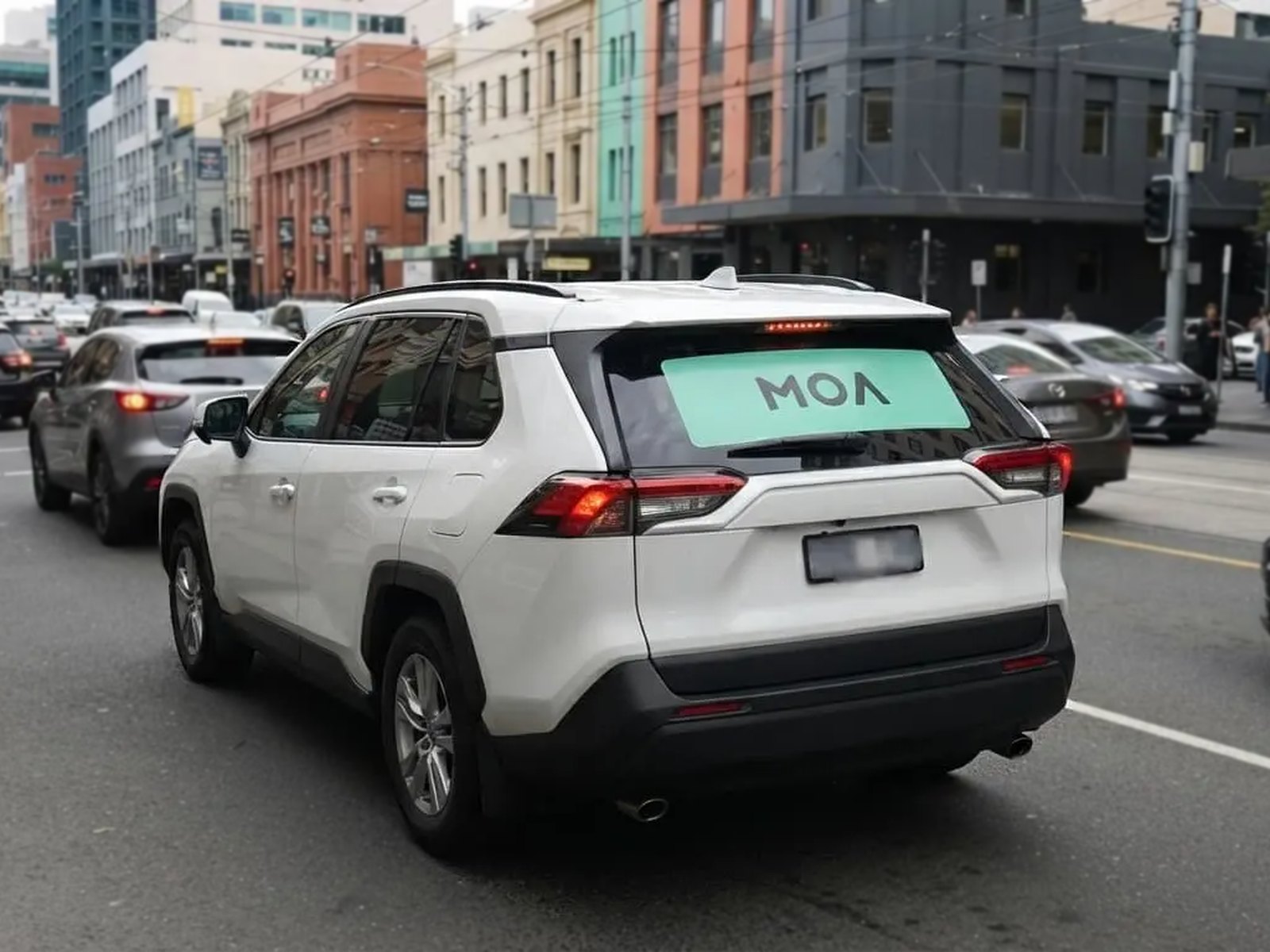 MOA branded white SUV in dense city traffic, rear window ad visible